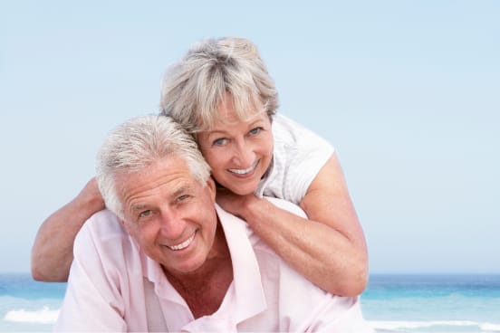 Happy couple smiling together at the beach, representative of patients after full-arch implant treatment